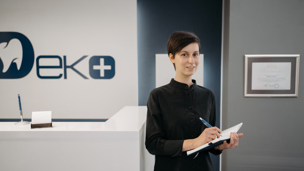Smiling woman holding a notebook at a modern dentist office reception area.